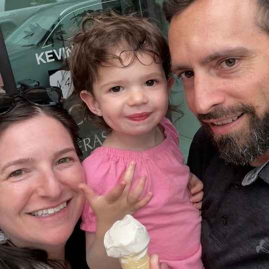 Family of three with a child holding an ice cream cone, standing in front of a store.
