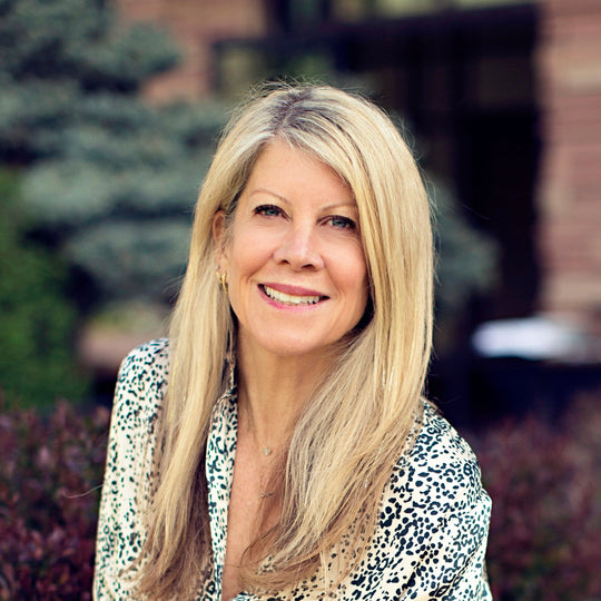 Woman sitting outdoors wearing a patterned blouse and white pants.